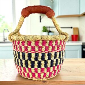 Small round Bolga basket with a bold chequered pattern in bright and dark tones and leather-wrapped handle