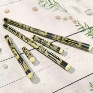 Bamboo rainsticks in multiple sizes, hand-painted with black and natural motifs, arranged on a white wooden surface.