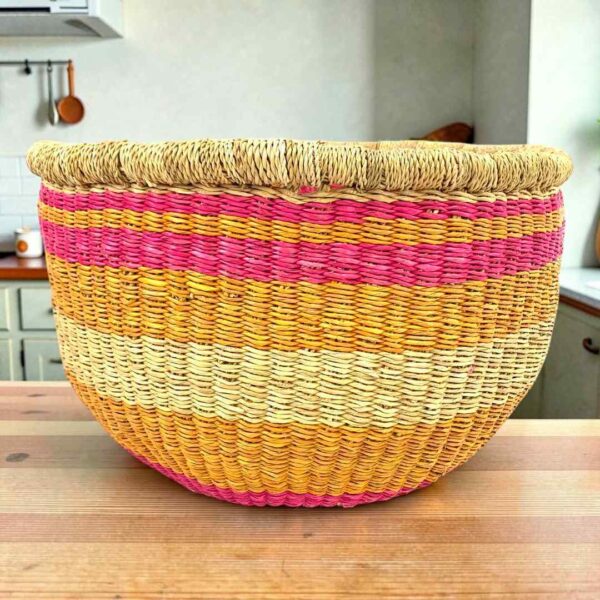 Round Bolga storage basket with pink, orange and yellow bands on natural straw and no handles