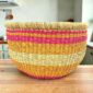 Round Bolga storage basket with pink, orange and yellow bands on natural straw and no handles