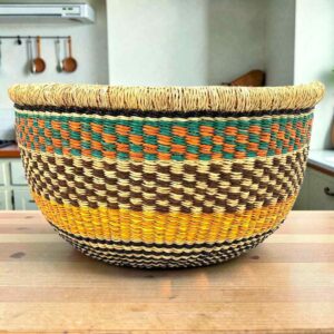 Round Bolga storage basket with a black and natural check, a mustard band and a teal and orange rim band, with no handles