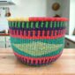 Round Bolga storage basket with teal, red, navy and green bands with a pale diamond band, and no handles