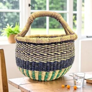 Vegan small round Bolga basket in blue tones with a woven elephant grass handle and a teal striped base, on a wooden table