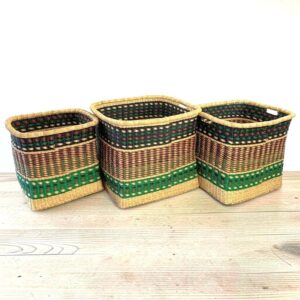 Three Vounu square baskets in black, brown and green stripes sitting side by side on a pale timber floor.