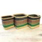 Three Vounu square baskets in black, brown and green stripes sitting side by side on a pale timber floor.