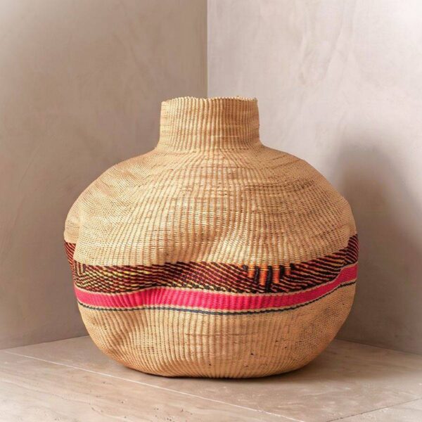 Bolga Wave Pot Basket in a natural elephant grass tone with a pink, orange and yellow wave band, styled in a sunlit corner