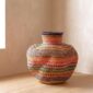 Bolga Wave Pot Basket in rust, olive green and pink woven bands, styled on a timber floor