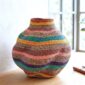Bolga Wave Pot Basket in teal, gold, rust, pink and purple woven bands, styled on a timber floor by a window