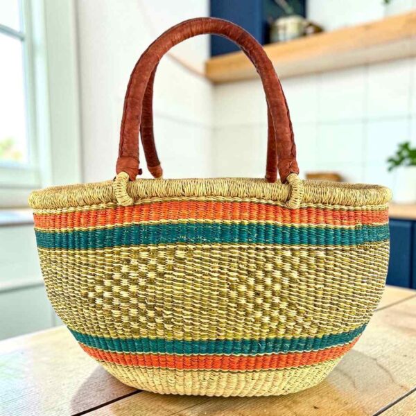 Orange and teal Mega Wawa Bolga basket with a checked natural centre panel and two leather handles, on a wooden table