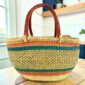 Orange and teal Mega Wawa Bolga basket with a checked natural centre panel and two leather handles, on a wooden table