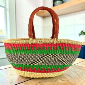 Red and green striped Mega Wawa Bolga basket with a black zigzag panel and two leather handles, on a wooden table