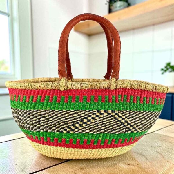 Red and green striped Mega Wawa Bolga basket with a black zigzag panel and two leather handles, on a wooden table