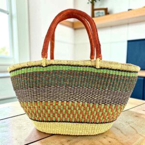 Mega Wawa Bolga basket in a speckled olive green and rust weave with two leather handles, on a wooden table