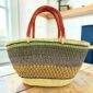 Mega Wawa Bolga basket in a speckled olive green and rust weave with two leather handles, on a wooden table