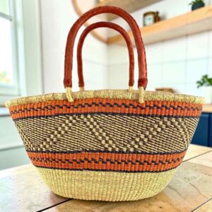 Mega Wawa Bolga basket with orange bands, a black and natural zigzag panel and two leather handles, on a wooden table