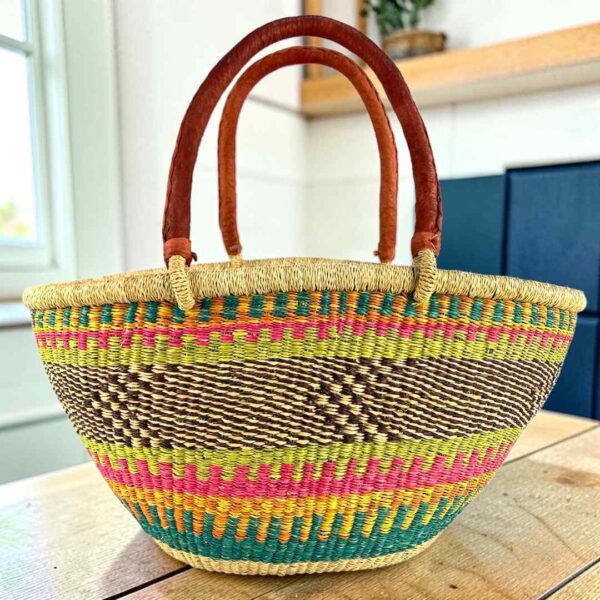Multicolour Mega Wawa Bolga basket with pink, green, orange and teal checked bands and two leather handles, on a wooden table