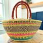 Multicolour Mega Wawa Bolga basket with pink, green, orange and teal checked bands and two leather handles, on a wooden table