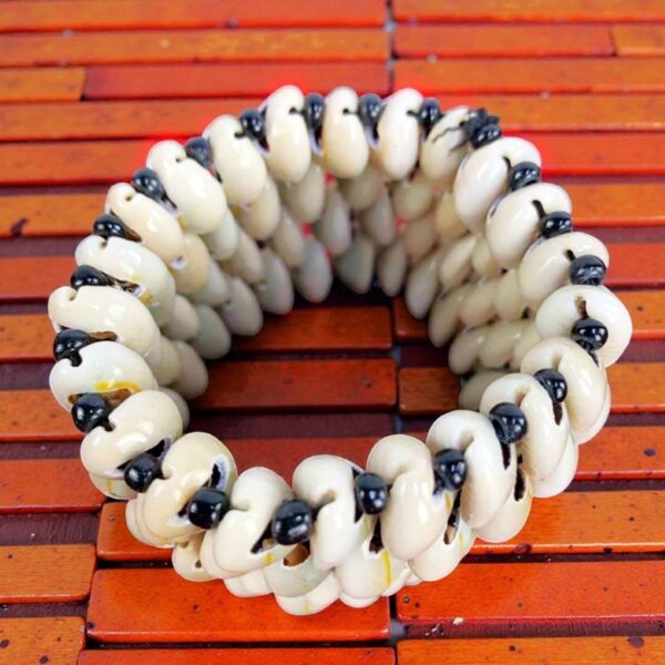 Handmade 4 strand cowrie shell bracelet flat lay showing white and black bead details on wood background