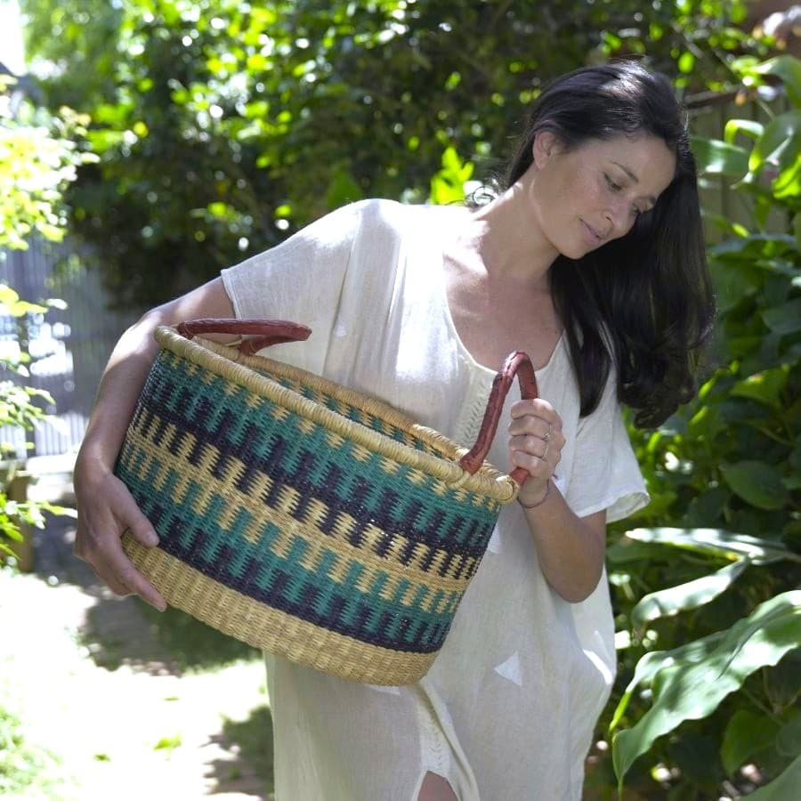 African hamper storage basket in blue tones, carried by a woman in a garden.